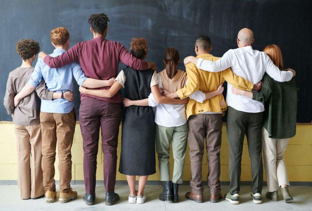 A diverse group of adults in casual outfits hugging in front of a chalkboard, symbolizing teamwork. Neurodiversité au travail
